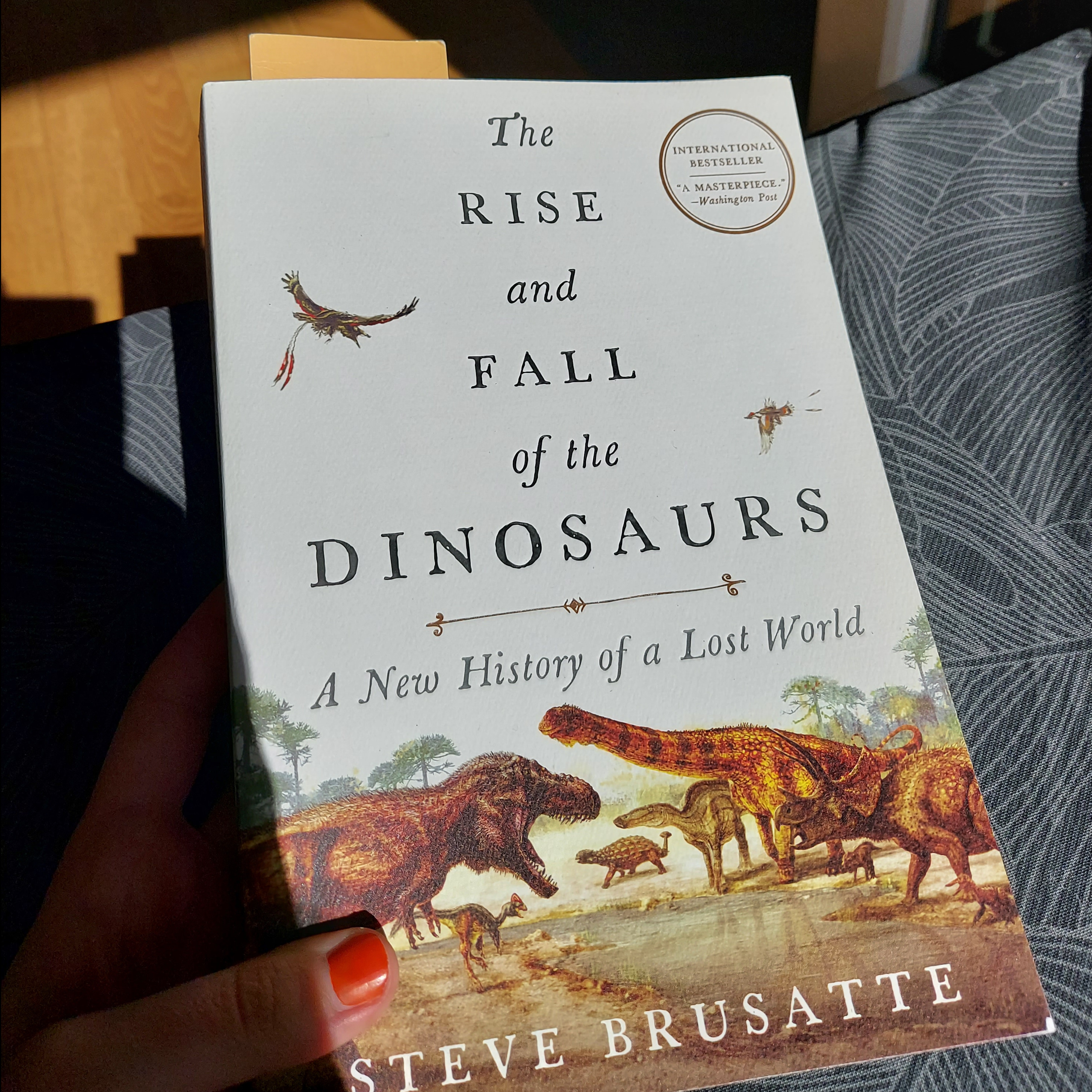 Me holding a book. It's 'The Rise and Fall of the Dinosaurs' by Steve Brusatte.